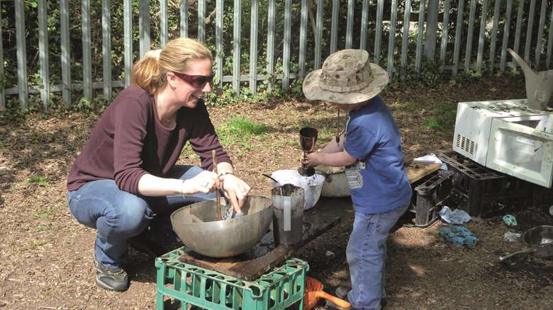 A parent joins their child in the mud kitchen